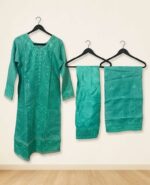 A woman modeling a premium sea green chomok silk kota embroidered stitched three-piece dress, showcasing detailed self-embroidery and sequin work on the neckline and hem, paired with a matching embroidered kota dupatta and soft silk trousers.