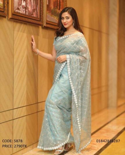 A woman modeling a light sky blue net saree with geometric sequin work and an embellished border.