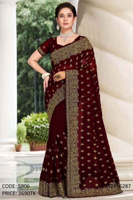 A woman modeling a beautiful maroon soft georgette saree featuring intricate golden embroidery and sequence work with a matching blouse.