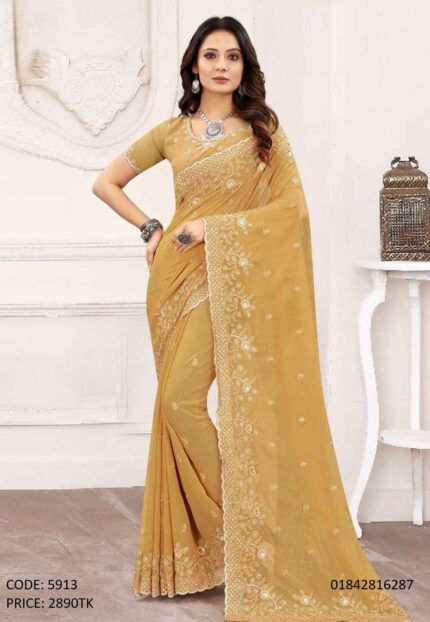A woman posing in a golden-mustard soft georgette saree featuring intricate embroidery and sequence work on the border and body.