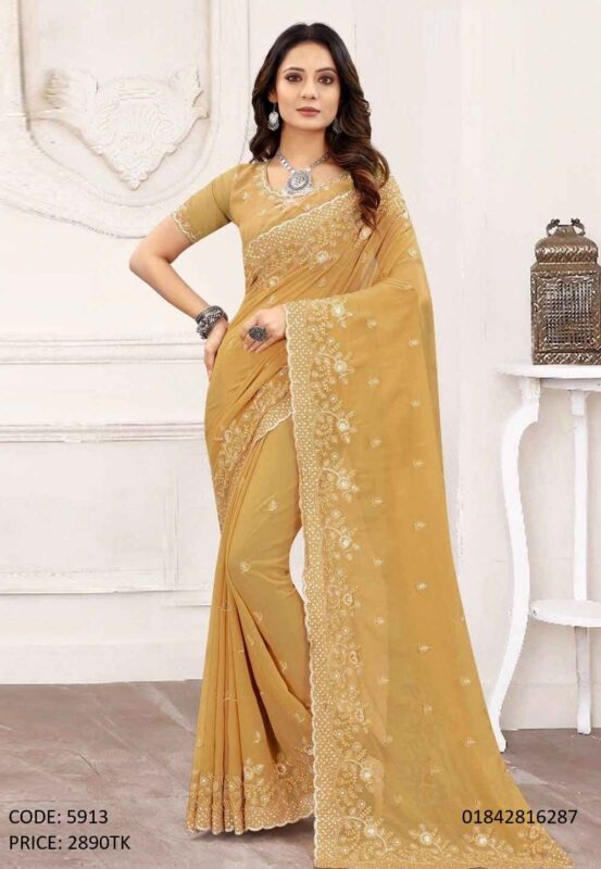 A woman posing in a golden-mustard soft georgette saree featuring intricate embroidery and sequence work on the border and body.